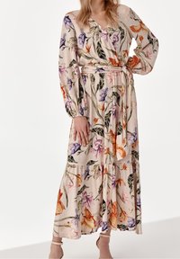 Blomster maxi kjole i lys beige stof, med lange ærmer, V-hals, talje med bælte og en lagdelt nederdel med flerfarvede blomstermønstre.