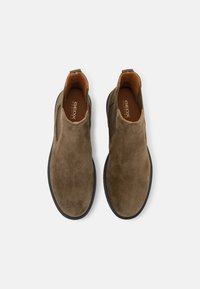 Ruske suede gležnjače s elastičnim bočnim panelima i crnom gumenom potplatom. Unutrašnjost ima bež podstavu i teksturiranu unutarnju oblogu.