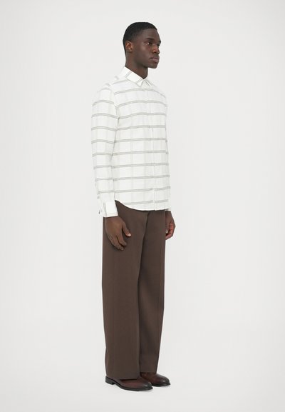 Witte overhemd met knopen en een rasterpatroon, gecombineerd met brede, bruine broekspijpen. Het overhemd heeft een klassieke kraag en lange mouwen.