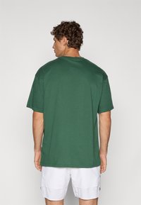 Grøn bomulds t-shirt med en afslappet pasform og korte ærmer, der har en rund halsudskæring og en glat tekstur, vist fra bagsiden.