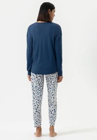 Haut à manches longues bleu marine avec un col arrondi, associé à un pantalon de pyjama blanc imprimé floral dans des nuances de bleu et de marine. Tissu en mélange de coton doux.