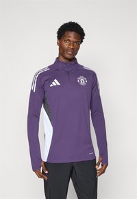 Purple long-sleeve athletic top with half-zip, Manchester United logo, white and black side accents, and textured fabric inserts.