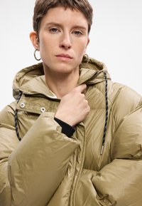 Maslinasto zelena puf jakna s kapuljačom, s zatvaračem na zip, podesivim šnurlama i sjajnom, glatkom teksturom.