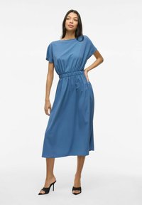Rochie midi albastră cu mâneci scurte, talie elastică, textură netedă și croi lejer. Asortată cu toc înalt, negru, cu vârf descoperit.