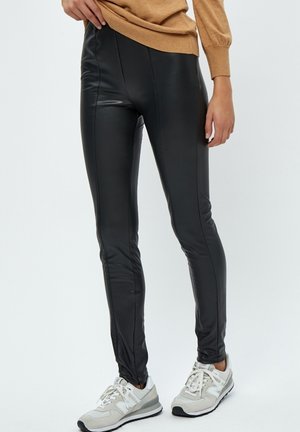 Leggings in ecopelle nera con una vestibilità slim, caratterizzati da cuciture verticali per dare forma, abbinati a scarpe da ginnastica grigio chiaro.