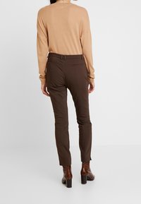 Bruine slim fit broeken met een gladde structuur, voorzakken en een riemdetail, gecombineerd met een tan langemouwen top en bruine haklaarzen.
