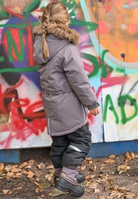 Harmaa eristetty parka, jonka reunassa on tekoturkista, säädettävä vyötärö, yhdistetty mustiin vedenpitäviin housuihin ja ruskeisiin talvikenkiin.