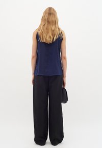 Mjörkt ärmad topp i marinblått, kombinerad med svarta vida byxor. Modellen håller en liten svart handväska och vänder sig bort från kameran.