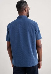 Cămașă cu mânecă scurtă, de culoare albastră închisă, cu dungi verticale, realizată dintr-un material texturat. Prezintă un guler la gât și o croială relaxată.