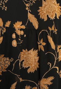 Svart tyg med intrikata gyllene blomsterbroderier, inklusive blad och kronblad, samt en rynkad sömdetalj.