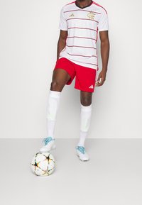 White and red striped football jersey, red shorts, and white socks with a blue and white soccer ball at foot. Materials: synthetic fabric.