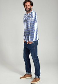 Langærmet stribet skjorte i hvid og blå bomuld, parret med mørke denimjeans og brune ruskindsko. Enkel design og afslappet pasform.