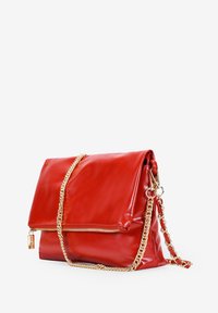 Bolso de mano de cuero rojo con diseño plegable, que presenta una correa de cadena dorada para el hombro y un compartimento con cremallera en la parte frontal.
