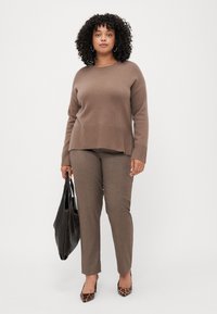 Brun strikkegenser med ribbestrikket kant, kombinert med brune skreddersydde bukser. Tilbehør inkluderer en svart tote bag og pumps med leopardmønster.