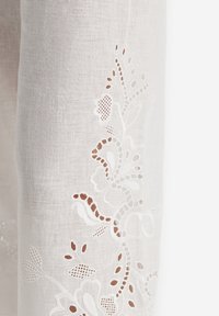 Vitt broderat tyg med blommönster, utskärningar och delikata texturer som ger ett luftigt och lätt utseende.