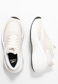 Reebok-sneakers i beige mesh och läder, med vita accenter och en texturerad svart sula. Dämpad sula för komfort och stöd.