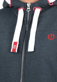 Dark gray zip-up hoodie made of soft material. Features white drawstrings with red accents, a small logo, and a metal zipper.