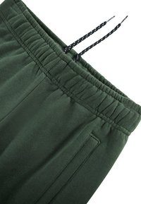 Mørkegrønne sweatpants med elastisk talje, der har en snor med sort-hvide polka-dots og sidelommer. Blød tekstur.
