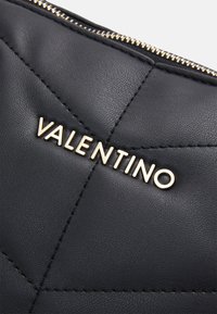 Black quilted leather bag with gold zipper and gold Valentino logo letters on the front.