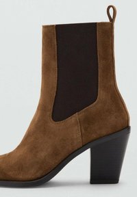 Ghetuță maro din piele întoarsă, cu părți elastice negre pe lateral, vârf ascuțit și toc pătrat. Dispune de o buclă la spate pentru a fi ușor de încălțat.