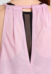 Top sin mangas de color rosa con un diseño de malla texturizada, que presenta un panel de malla negro y una abertura en la parte trasera con un ojal asegurado con un pequeño lazo.
