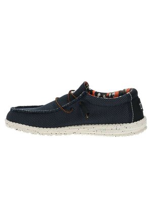 Scarpa slip-on in tessuto blu navy con tomaia strutturata, suola bianca maculata in contrasto e foderato interno a fantasia. Presenta un lacci di accento arancione.