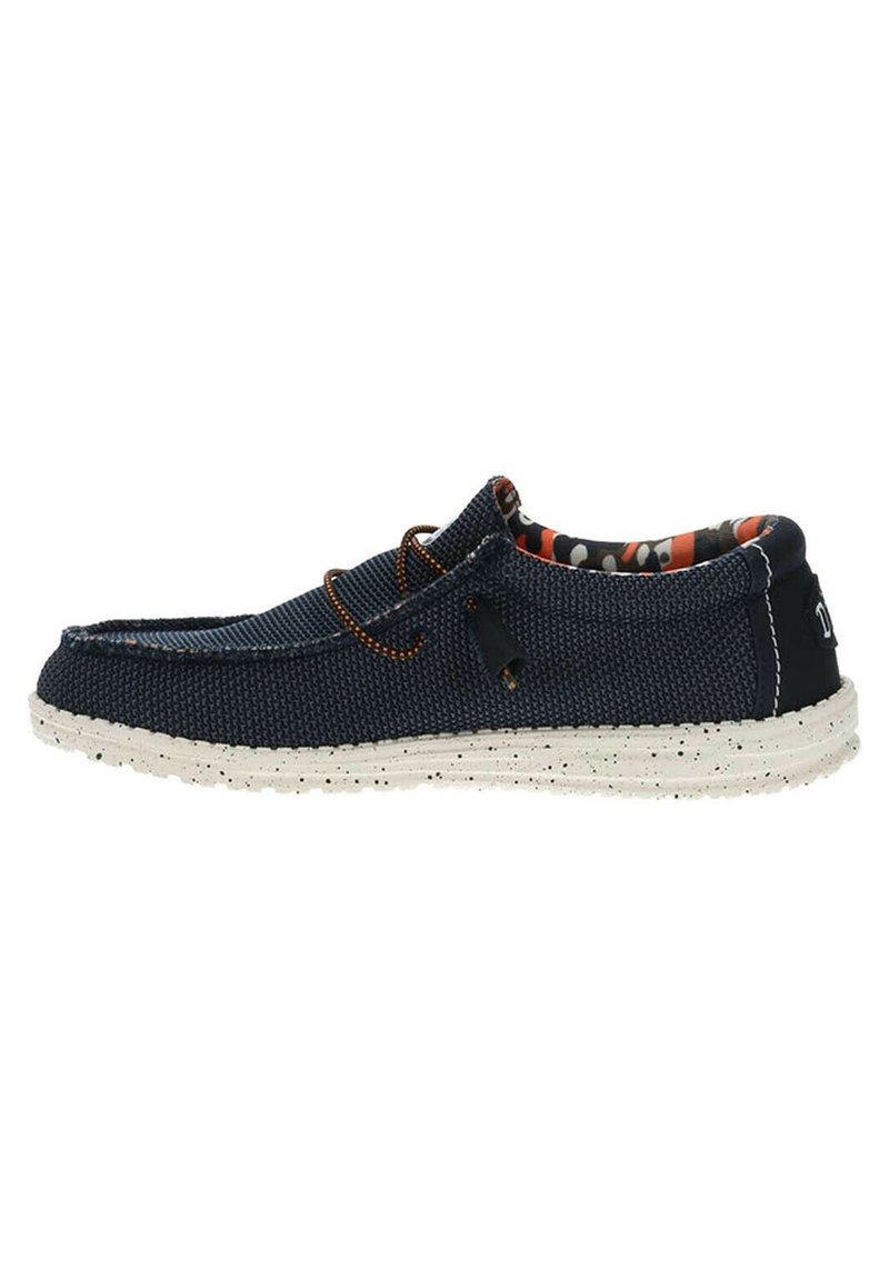 Zapato de lona azul marino sin cordones con una parte superior texturizada, suela blanca moteada contrastante y forro interior estampado. Cuenta con un cordón de acento naranja.
