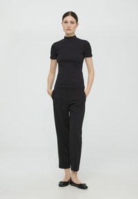 Czarny top z krótkim rękawem o wysokiej szyi, dopasowany krój, w połączeniu z czarnymi spodniami typu tailor oraz czarnymi baletkami. Gładka tekstura materiału.