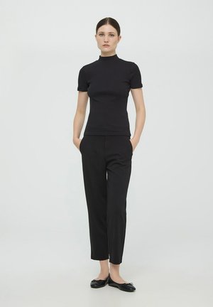 Top nero a maniche corte con collo alto, design aderente, abbinato a pantaloni neri sartoriali e ballerine nere. Tessuto dalla consistenza liscia.