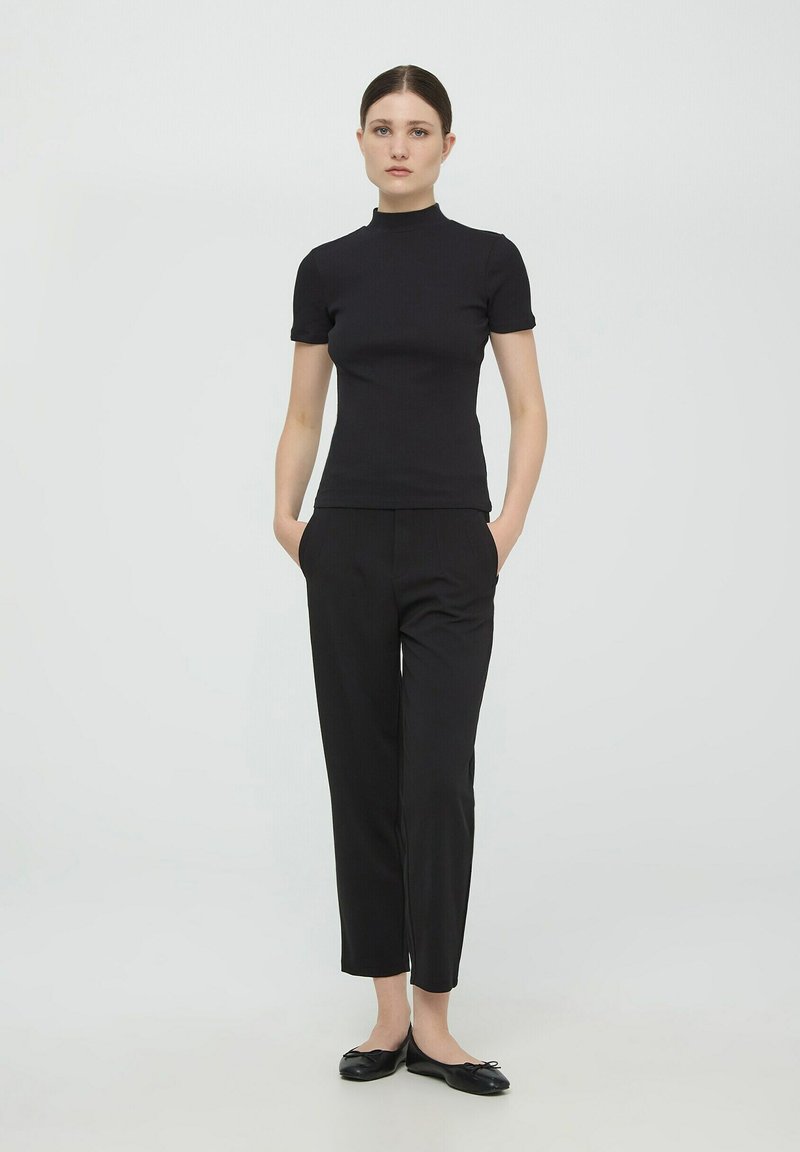 Czarny top z krótkim rękawem o wysokiej szyi, dopasowany krój, w połączeniu z czarnymi spodniami typu tailor oraz czarnymi baletkami. Gładka tekstura materiału.