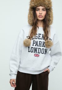 Šedá mikina s potiskem "Regent's Park London" v černé barvě, doplněná malou vlajkou Union Jack. V kombinaci s čepicí z umělé kožešiny s bambulemi.