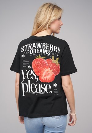 T-shirt noir avec un design graphique de fraises et un texte disant "Rêves de Fraises" et "oui, s'il vous plaît." Manches courtes, coupe décontractée.