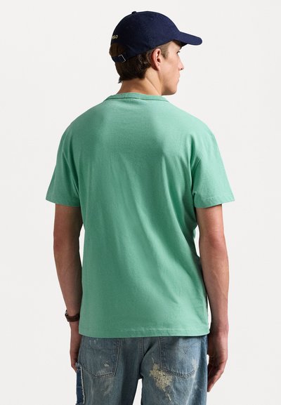 Mintgrön kortärmad T-shirt med rundad halsringning. Bärs med slitna ljusblå jeans. Marinblå keps med logotyp på baksidan.