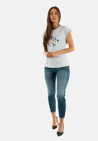 T-shirt azzurro chiaro a maniche corte con stampa floreale e geometrica. Abbinalo a jeans blu sbiaditi e tacchi neri. Tessuto con una consistenza morbida.