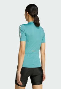 Turquoise cycling jersey with short sleeves, seamless construction, and reflective accents, paired with black padded cycling shorts.