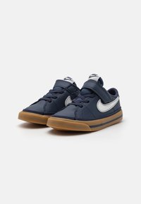 Baskets bleu marine avec une tige en synthétique lisse, logo swoosh blanc, semelle extérieure en caoutchouc gourmand contrastante et sangle Velcro réglable.