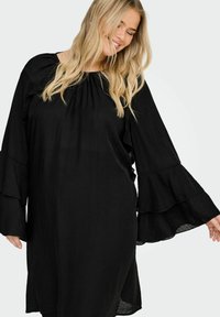 Crna haljina dugih rukava s volanima i laganom, teksturiranom tkaninom. Izrez je elastičan za opušteno pristajanje.
