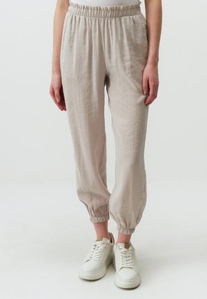 Pantaloni beige chiari con vita elastica e caviglie arricciate, realizzati con un tessuto testurizzato, abbinati a sneaker bianche.