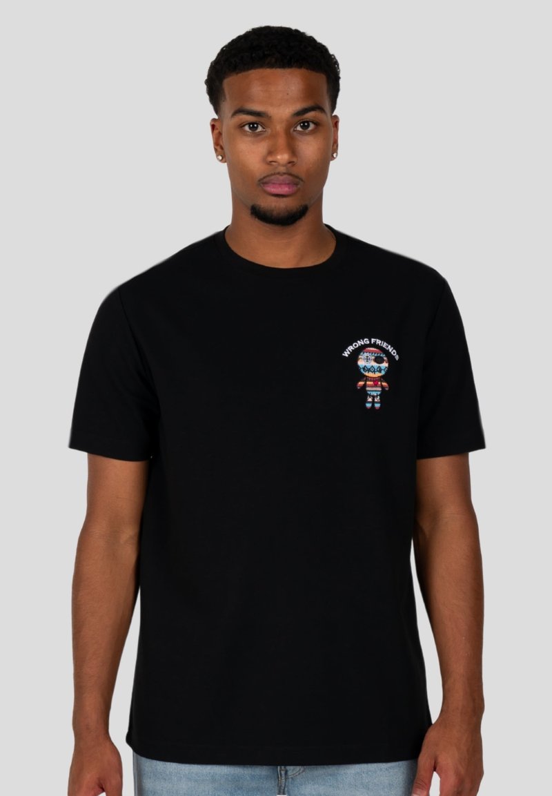 Schwarzes Baumwoll-T-Shirt mit einem bunten gestickten Charakter und dem Text "FALSCHE FREUNDE" auf der oberen linken Seite. Kurze Ärmel.