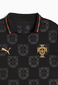 Črna polo majica z teksturiranimi nacionalnimi grbi, zlatim logotipom Puma in ovratnikom z rdečimi ter zelenimi poudarki in črtami.