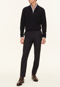 Pull en maille bleu marine avec une fermeture éclair quart, associé à un pantalon noir ajusté et des chaussures en cuir marron foncé. Lignes épurées et textures lisses.