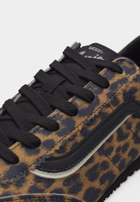 Κοντινό πλάνο καφέ και μαύρου αθλητικού παπουτσιού με λεοπάρ σχέδιο, μαύρα κορδόνια και μαύρη ρίγα κατά μήκος της πλευράς.