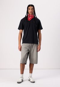 Tricou din bumbac negru, pantaloni scurți din denim gri, bentiță roșie și pantofi sport albi cu accente negre. Modelul stă pe un fundal deschis.
