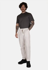 Camiseta gris de manga corta combinada con pantalones blancos con cordón y zapatillas negras. Los pantalones tienen un ajuste holgado y una tela texturizada.