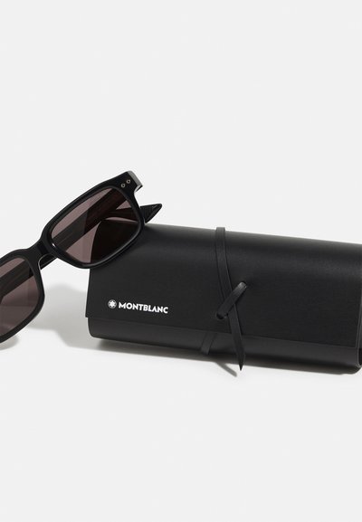 Occhiali da sole Montblanc neri con montatura rettangolare, lenti scure e finitura opaca, posizionati accanto a un astuccio cilindrico nero con un nastro.