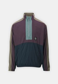 Pullover jacket in purple, navy, and light blue. Features a high collar, half-zip front, elastic cuffs, and an adjustable waistband.