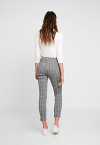 Pantaloni grigi a quadri a vita alta con una vestibilità slim, caratterizzati da una texture di tessuto liscia e un orlo corto, abbinati a sneakers bianche.
