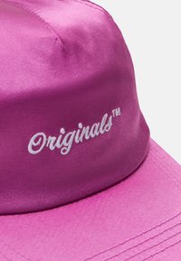 Růžová saténová čepice s bílým vyšívaným textem "Originals™." Design obsahuje strukturovanou korunu a zahnutý kšilt.