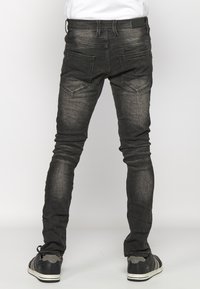 Black denim jeans with a slim fit, featuring back pockets, subtle fading, and a smooth texture. Paired with black and gray sneakers.