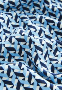 Tessuto blu e bianco con un motivo geometrico caratterizzato da forme triangolari e tonalità di blu che variano su uno sfondo blu navy.